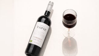 Fles Château Tapie Languedoc rode wijn met een gevuld wijnglas op een lichte ondergrond.