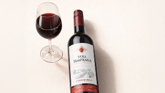 Fles rode wijn Viña Temprana Campo de Borja met een gevuld wijnglas ernaast op een lichte ondergrond.