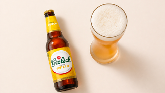 Fles Grolsch Puur Weizen naast een vol glas witbier op een lichte ondergrond.