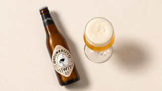 Fles Brouwerij ’t IJ IJwit 6,5% en een bijpassend glas witbier met schuimkraag op een lichte achtergrond.