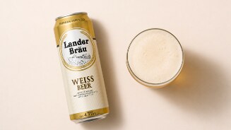 Blik Lander Bräu Weissbier naast een glas bier met schuimkraag op een lichte ondergrond