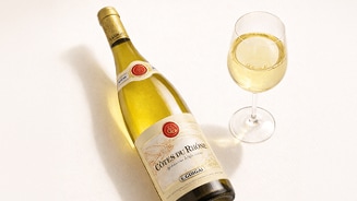 Fles en glas witte wijn Côtes du Rhône van het merk E. Guigal op een lichte ondergrond