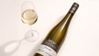Fles Divino Weisser Burgunder witte wijn en een gevuld wijnglas op een lichte ondergrond