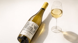 Fles Rustenberg Chardonnay en een glas witte wijn op een lichte ondergrond