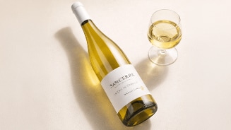 Fles Sancerre witte wijn met een gevuld wijnglas ernaast op een lichte ondergrond.