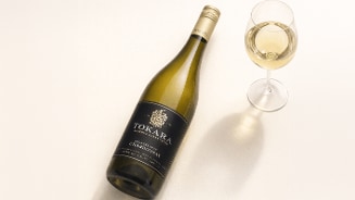Fles Tokara Chardonnay wijn met een gevuld wijnglas op een lichte ondergrond