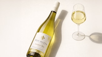 Fles Touraine Sauvignon Blanc met een gevuld glas witte wijn op een lichte ondergrond