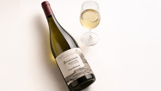 Fles Zuccardi Chardonnay witte wijn naast een gevuld wijnglas op een lichte achtergrond