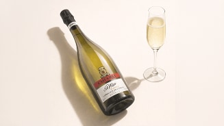 Fles Chiarli Lambrusco Dell’Emilia wijn naast een glas mousserende wijn op een lichte achtergrond.