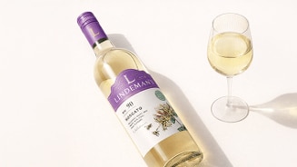 Fles Lindeman's Moscato witte wijn met een glas ingeschonken wijn ernaast op een lichte ondergrond