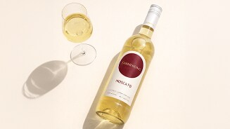 Fles Sarmentino Moscato witte wijn en een glas met ingeschonken wijn op een lichte ondergrond