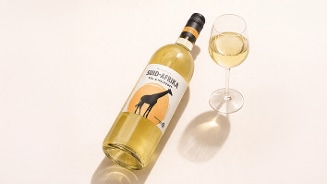 Fles Zuid-Afrikaanse witte wijn en een gevuld wijnglas op een lichte ondergrond