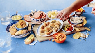 Borrelplank met diverse hapjes, waaronder kaasblokjes, droge worst, brood, toastjes, gevulde broodjes, dips, augurken, tomaatjes en een hand die een hapje pakt.