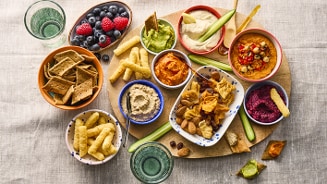 Een borrelplank met diverse dips, crackers, chips, groentesticks, notenmix en een schaaltje met blauwe bessen en frambozen.