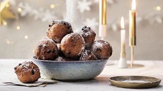Schaal met oliebollen met poedersuiker en kaarsjes op de achtergrond