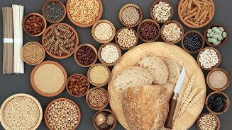 Verschillende kommen met granen, peulvruchten en zaden naast een gesneden brood op een houten snijplank met mes.