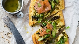 Platbrood belegd met gerookte zalm en groene asperges, geserveerd met een groen kruidenolie.