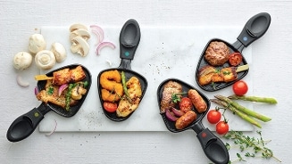 Gourmet pannetjes gevuld met verschillende soorten vlees, groenten en kruiden op een witte ondergrond, omringd door champignons, uienringen en cherrytomaten.