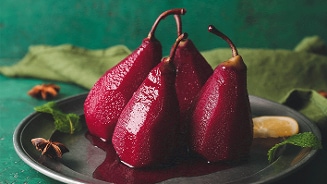 Gestoofde stoofperen op een bord, omringd door specerijen en munt, tegen een groene achtergrond