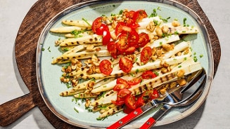 Gegrilde witte asperges met cherrytomaten, gehakte noten en verse kruiden, geserveerd op een schaal.