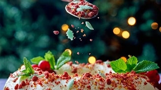 Decoratieve kersttaart bestrooid met rode en groene sprinkles, voorzien van muntblaadjes.