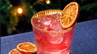 Glas roze cocktail met ijs, gegarneerd met schijfjes gedroogde sinaasappel.