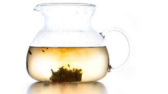 Glazen theepot met hete thee en losse thee bladeren.