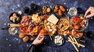Gezellig gedekte tafel met diverse kazen, vleeswaren, hapjes en macarons op een blauwe ondergrond.