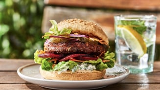 Burger met sla, rode ui, augurken, wortel en saus op een houten tafel met een glas water met citroen.