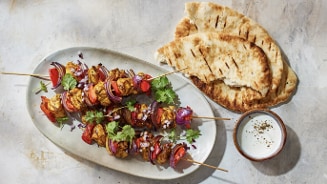 Geroosterde groentespiesjes met paprika en rode ui, geserveerd met naanbrood en een kom dipsaus.