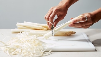 Hand schilt witte asperges op een snijplank.