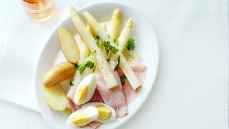 Bord met witte asperges, gekookte aardappelen, ham en een gehalveerd hardgekookt ei.
