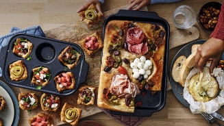 Feestelijke borrelhapjes met mini quiches, focaccia met vleeswaren en olijven, en gesmolten kaas met brood.