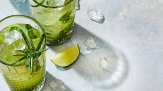 Verfrissende cocktail met ijs, munt en limoen in glazen, geserveerd met goudkleurige rietjes.