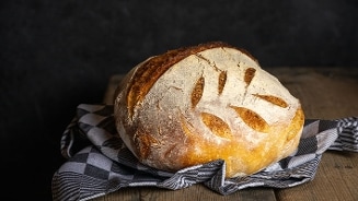 Ambachtelijk rond brood met krokante korst op een houten tafel en geruit keukendoek