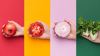Vier handen die respectievelijk een granaatappel, een gehalveerde tomaat, een plak rode ui en verse paksoi vasthouden op gekleurde achtergronden