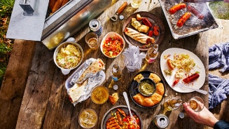 Volle buitentafel met gegrild vlees en salades tijdens een zomerse BBQ, net aangestoken
