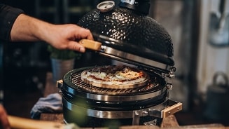 Houtskoolbarbecue met geopende deksel en een pizza die erin gebakken wordt.