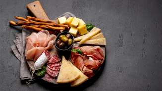 Antipasti plank met diverse kazen, vleeswaren, olijven en grissini.