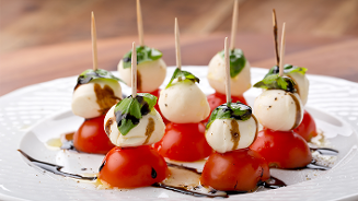 Caprese hapjes met cherrytomaten, mozzarella bolletjes en verse basilicum, besprenkeld met balsamico, op een bord.