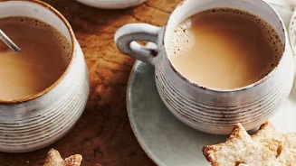 Twee kopjes koffie met melk en stervormige koekjes op een houten tafel.