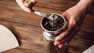 Handmatige koffiemolen met koffiebonen wordt bediend op een houten ondergrond.