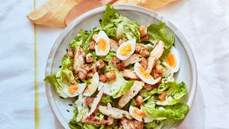 Caesarsalade met kip, croutons en stukjes ei op een witte bord.