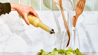 Hand giet dressing uit een fles over een salade in een kom