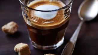 Espresso in een glas met klontjes bruine suiker en een lepel ernaast.