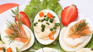 Gevulde eieren met mayonaise, bieslook, dille en gerookte zalm, geserveerd op sla met aardbeien.