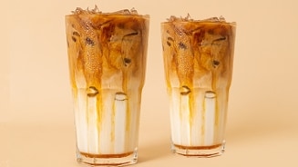 Twee glazen iced latte met melk en koffie op een beige achtergrond