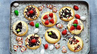 Versierde kerstkoekjes op een dienblad, omringd door chocolade kerstmannetjes en gekleurd snoepgoed.