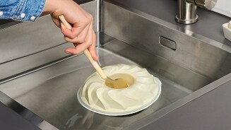 Een hand die een penseel vasthoudt om een bundt cakevorm schoon te maken in een gootsteen.