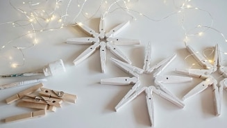 Sneeuwvlokken geknutseld van houten wasknijpers, wit geverfd en omringd door sfeervolle kerstverlichting op een witte ondergrond